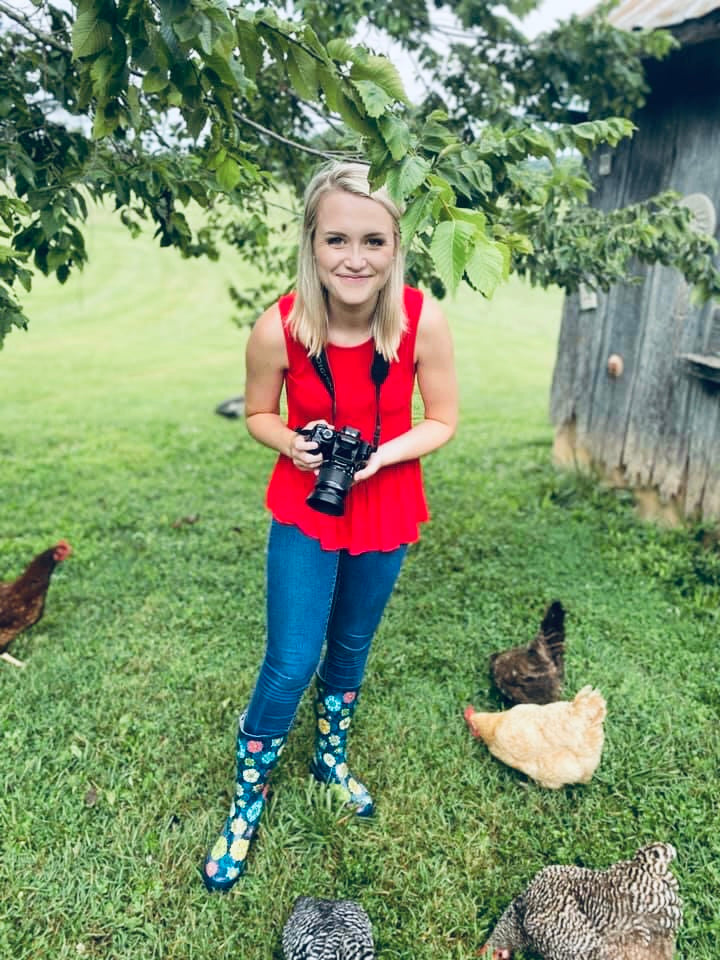 A girl smiles with a camera outside of her chicken coop