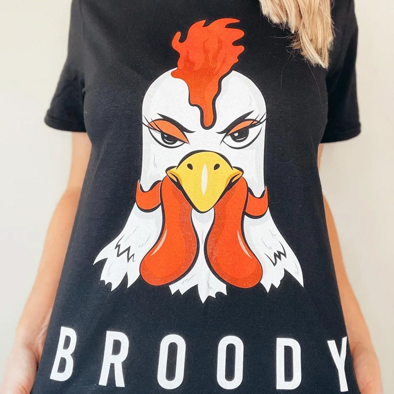 A girl wearing a black t-shirt with a chicken illustration on it with the words Broody